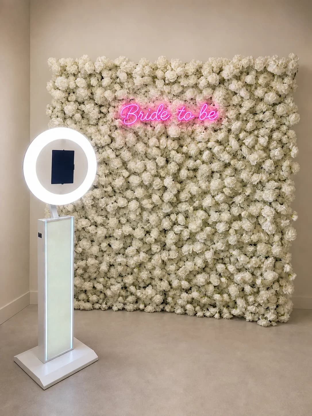 Rendered photo booth setup with a white ring-light booth in front of a white floral wall with a pink ‘Bride to be’ sign.